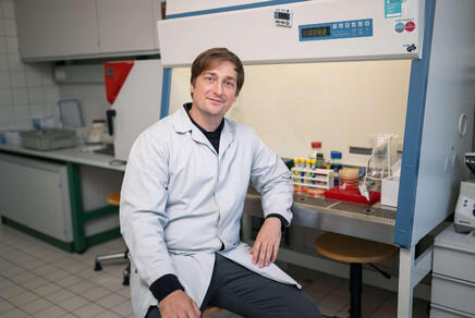 Laborleiter Patrick Mikuni-Mester sitzt im Labormantel gekleidet im Labor.