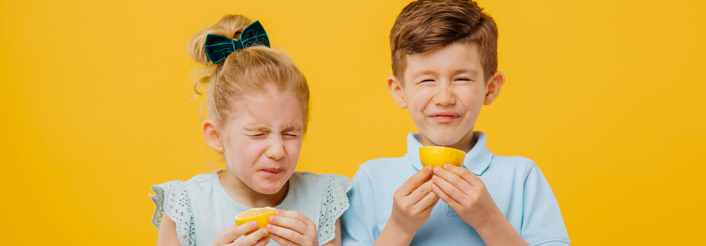 Ein Mädchen und ein Junge kosten eine Zitrone und verziehen ihr Gesicht.