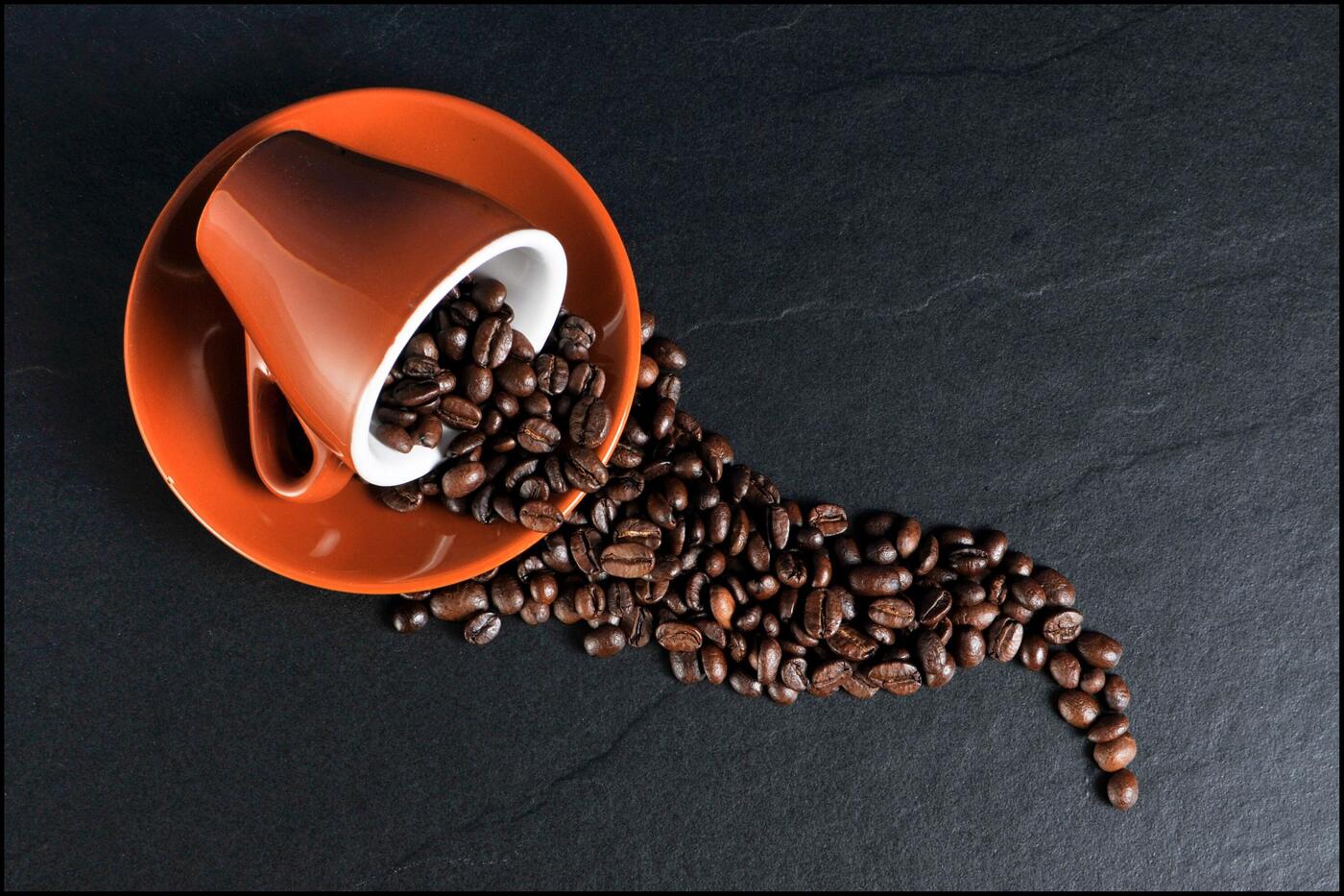 eine rostbraune Espressotasse umgefallen auf einer Untertasse, aus der Kaffeebohnen fließen.