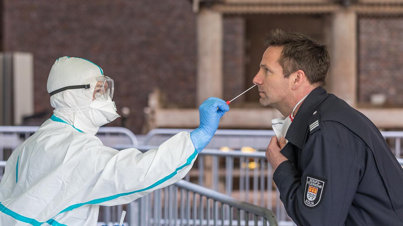 Eine Person in Schutzkleidung entnimmt einen Nasen-Rachen-Abstrich eines Mannes
