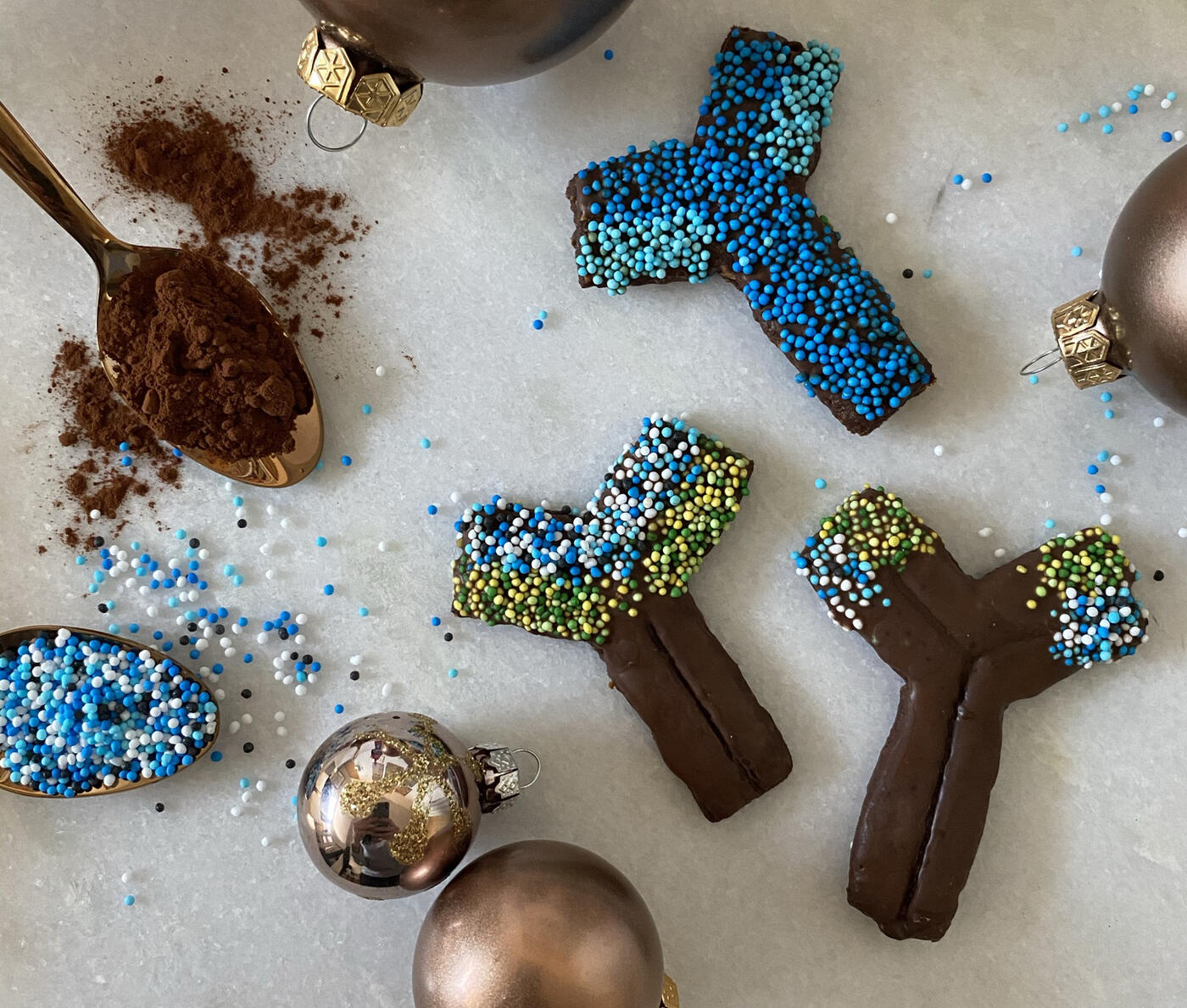 gebackene Schokoladen-Antikörper-Kekse mit Streuseln und Kakaopulver auf einem Löffel und Weihnachtskugeln