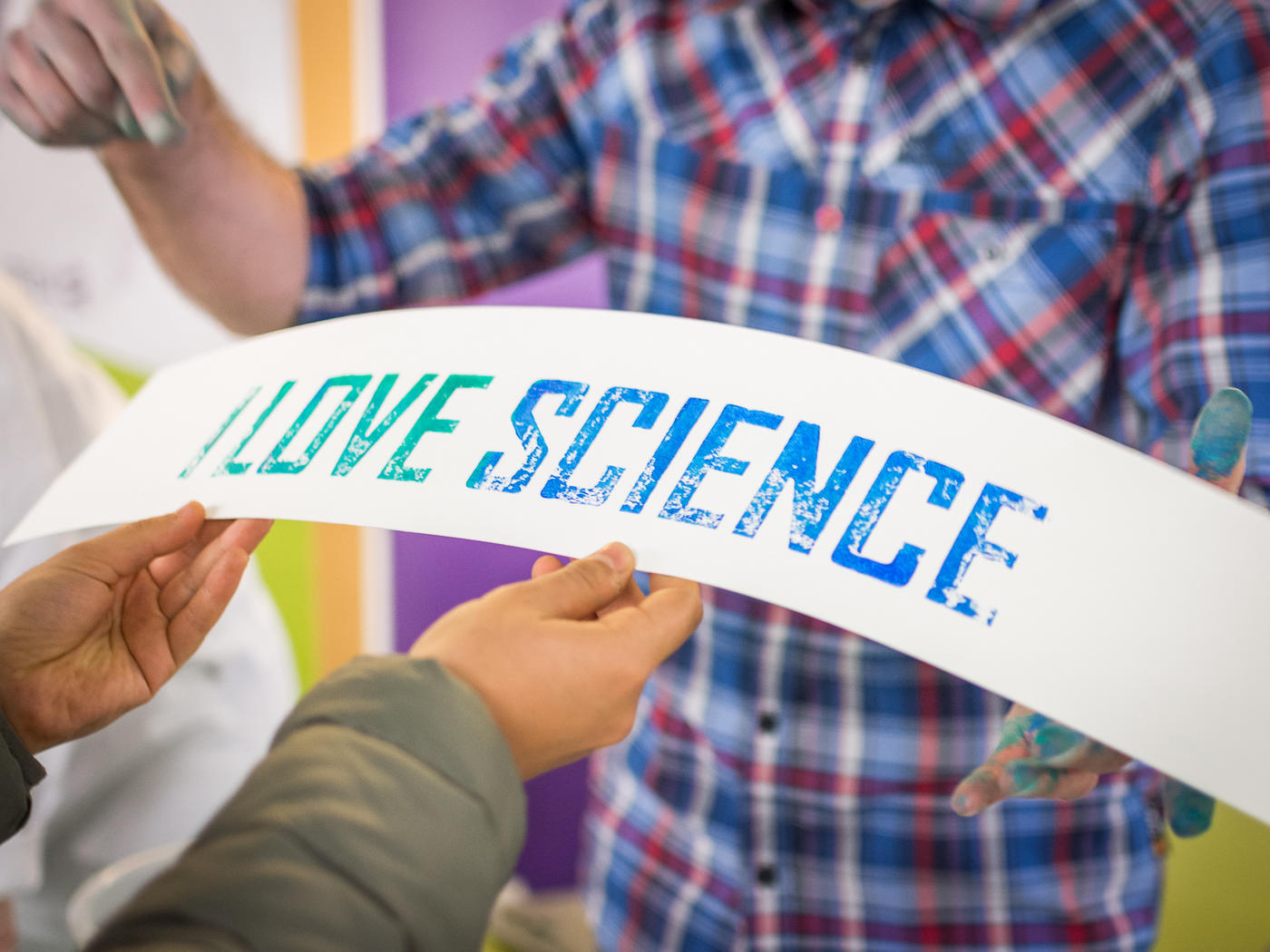 Auf dem Bild ist eine Person in einem karierten Hemd zu sehen, die auf einen Schriftzug "I love science" zeigt. 